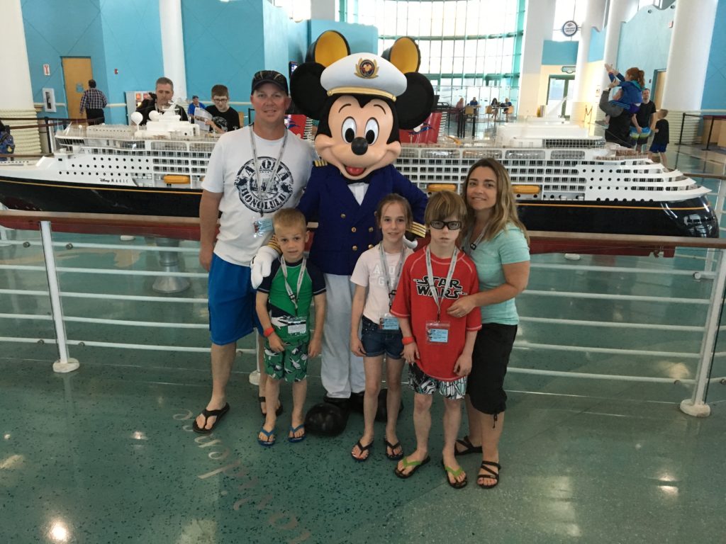 Family posing with Mickey Mouse before a cruise.