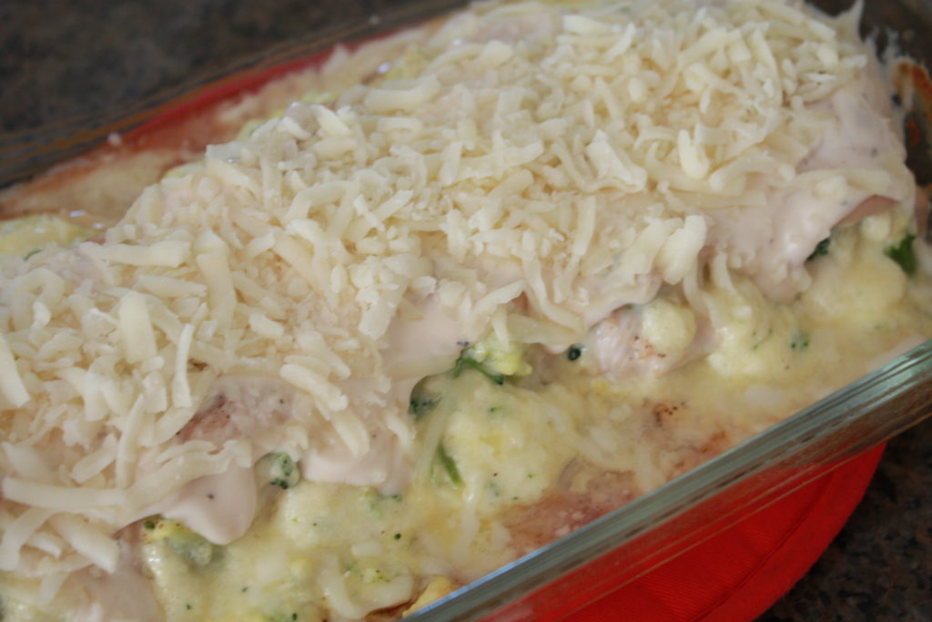 Adding alfredo sauce to the baking chicken. 