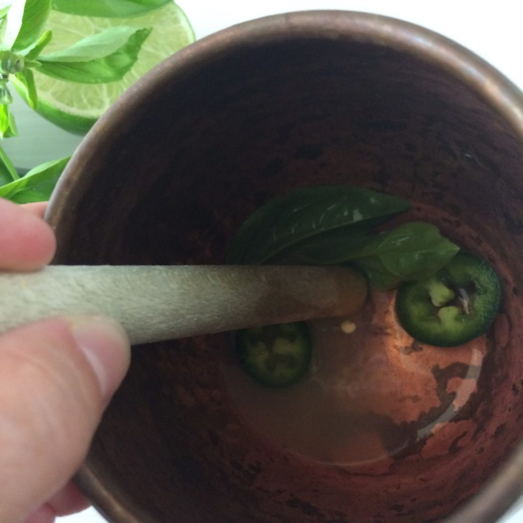 muddling the basil and fresh jalapeno slices in the copper mug