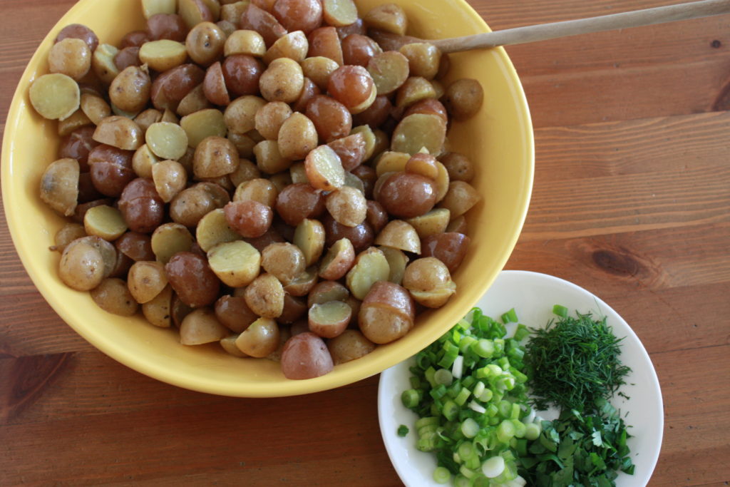 Toss potatoes with dressing next to another bowl filled with with chopped fresh herbs