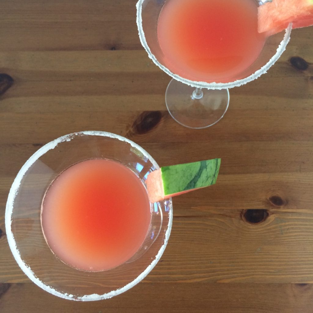 Two glasses of pink Watermelon mint martini garnished with mini wedges of the fruit.