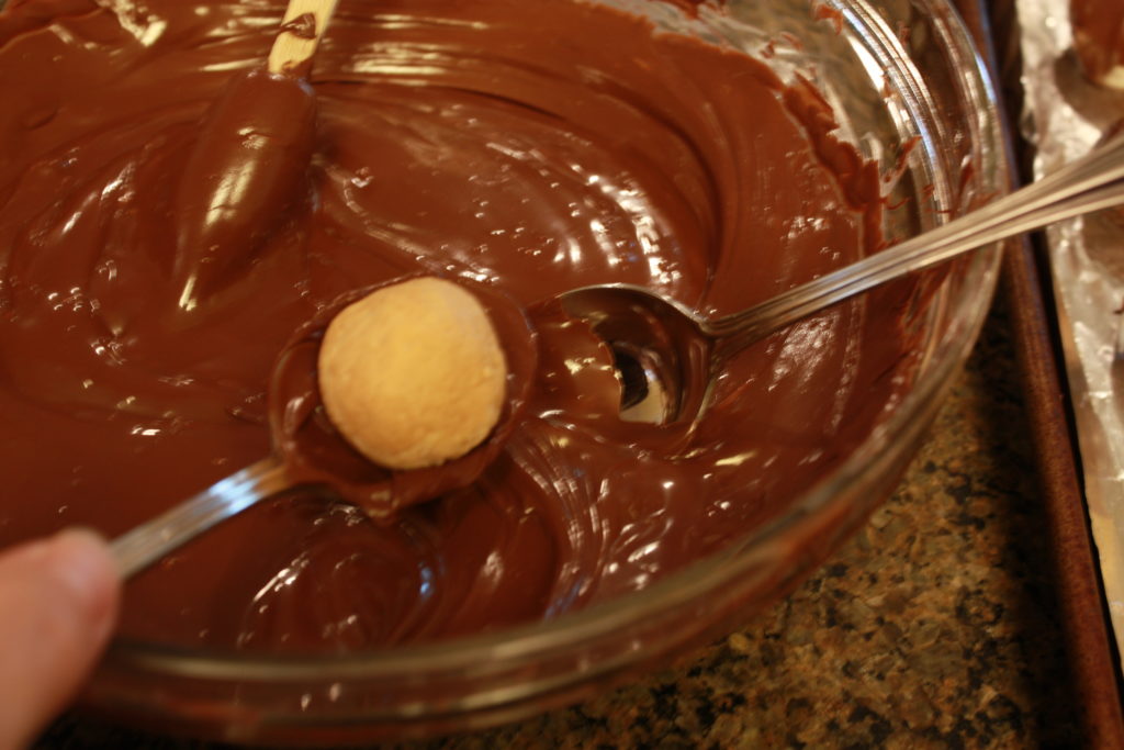 Small peanut butter balls on spoons to dip in chocolate