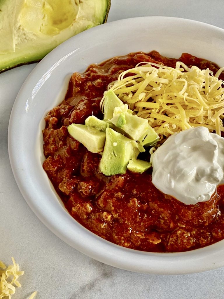 Slow Cooker Keto Beef & Bacon Chili without beans topped with avocado, cheese and sour cream.