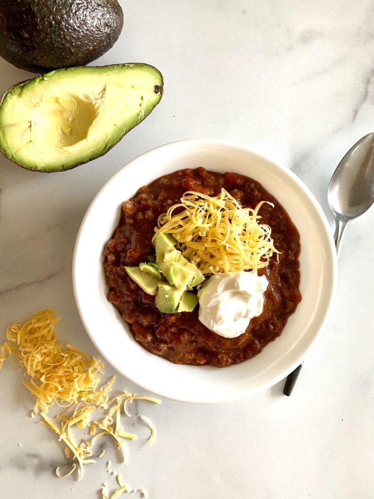 bowl of chili topped with cheddar, avocado, and sour cream