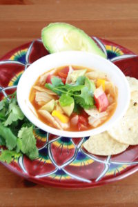 Slow Cooker Chicken Tortilla Soup in a bowl with chips, avocado, and cilantro
