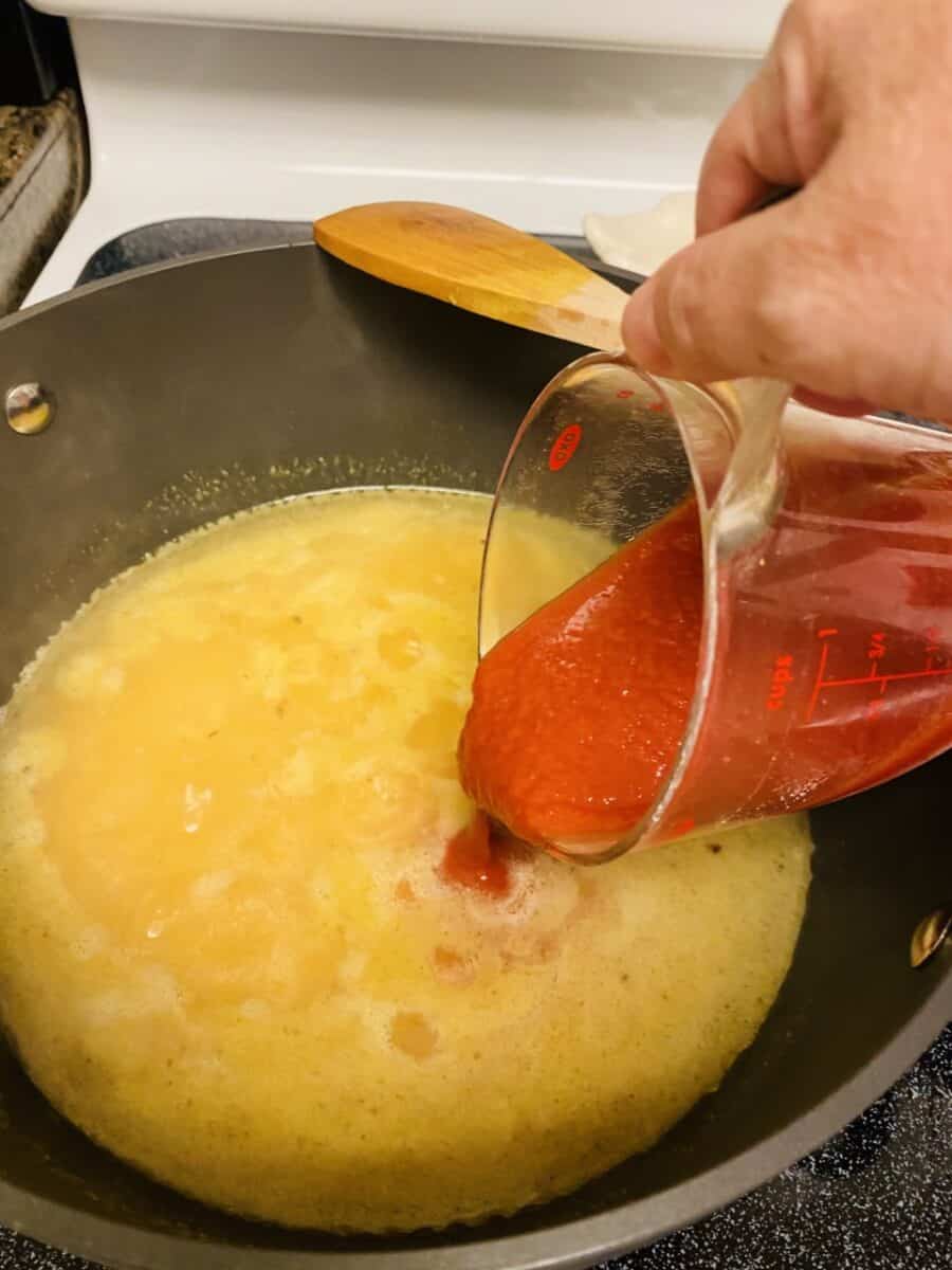 Adding broth and tomato sauce to pot.