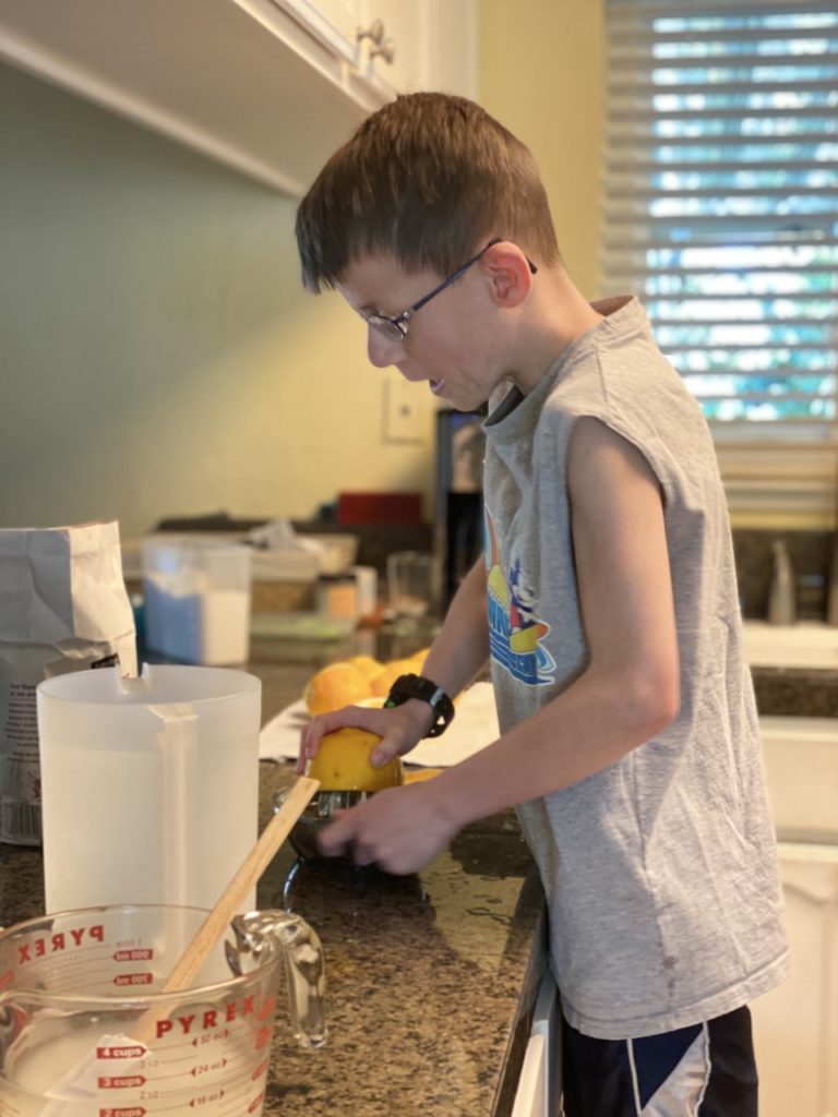 Child standing on a stool juicing lemons to make homemade lemonade concentrate. 