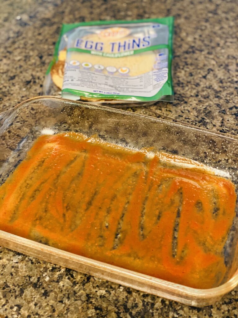 A large glass baking dish with some enchilada sauce on the bottom. 