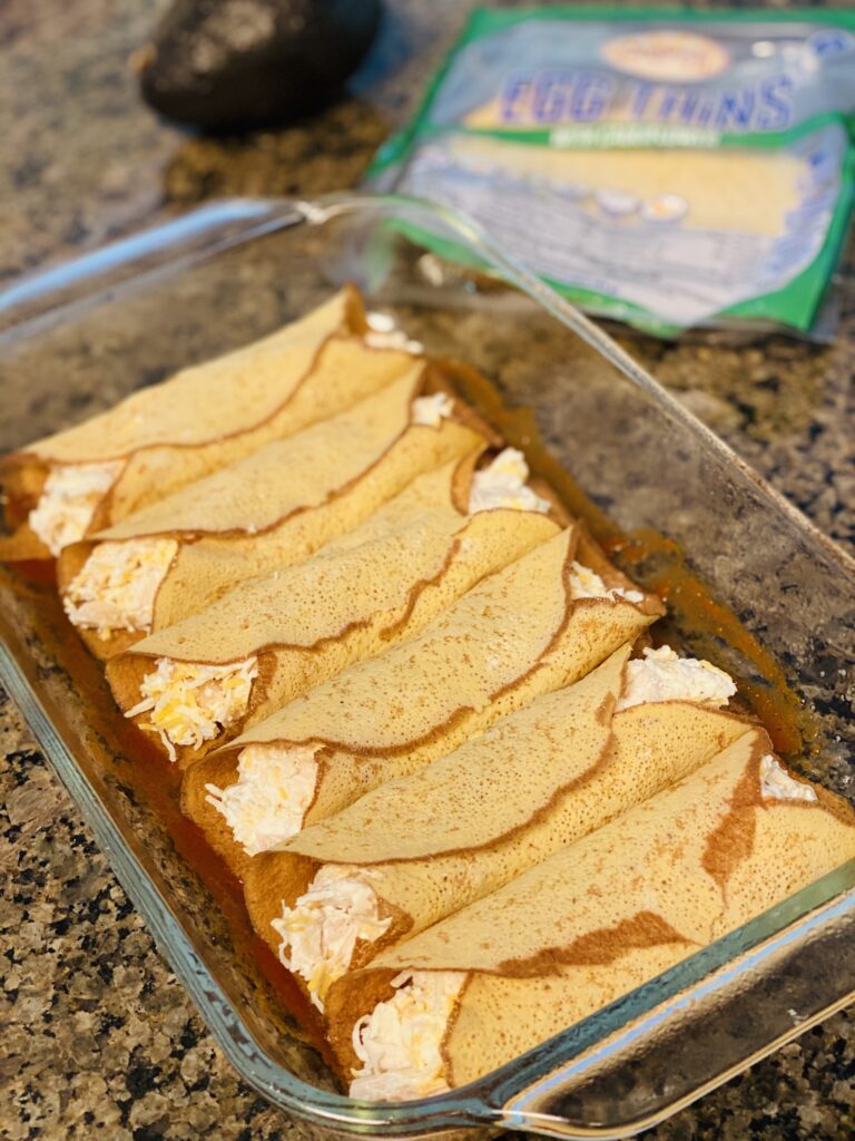 A baking dish is lined up with rolled enchiladas. 