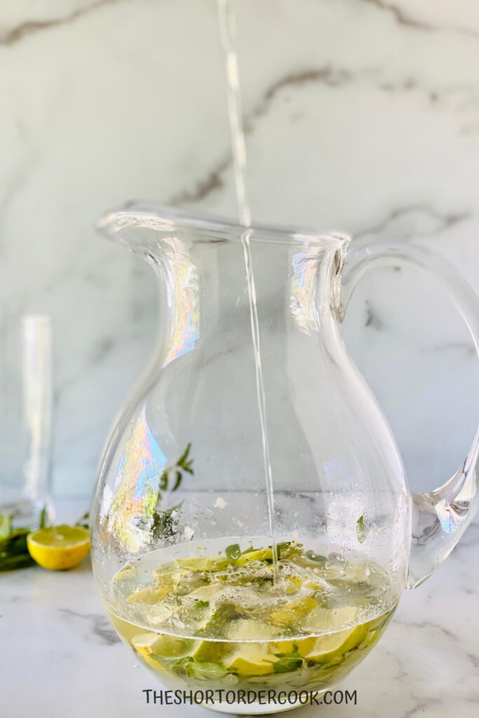 Club soda being poured into the pitcher of mojito run cocktail.