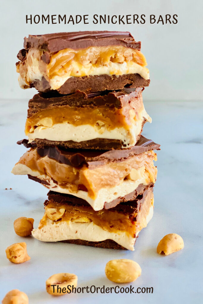 Homemade Snickers Bars stacked up with peanuts on the side. 