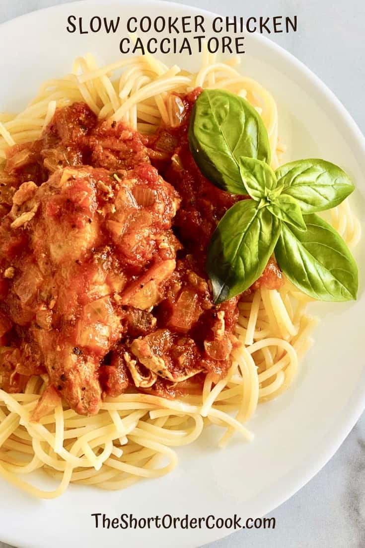 Chicken alla cacciatora over spaghetti on a plate with fresh basil leaves.
