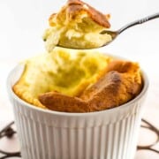 A white ramekin with baked cheese souffle and a spoon scooping out a bite