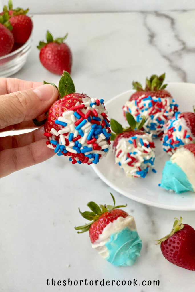 Red, White, & Blue Strawberries for 4th of July holding a white chocolate covered berry ready to eat