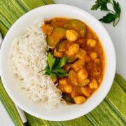 Zucchini, Chickpea, & Potato Curry featured overhead of bowl with curry and rice plus napkin spoon and parsley sprig recipe card image