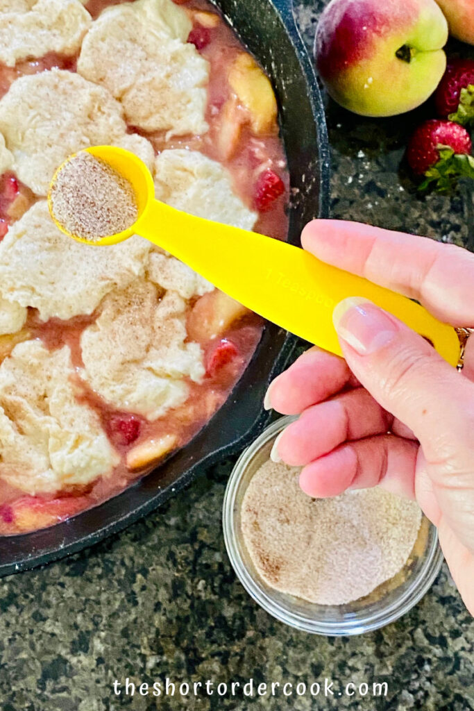 Old-Fashioned Skillet Peach & Strawberry Cobbler sprinkling the cinnamon sugar on top