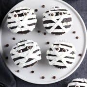 Vegan Halloween Treats & Drinks vegan-mummy-cupcakes-2 veganhuggs a plate with 4 chocolate cupcakes decorated with white crisscross and layered white frosting for a mummy effect