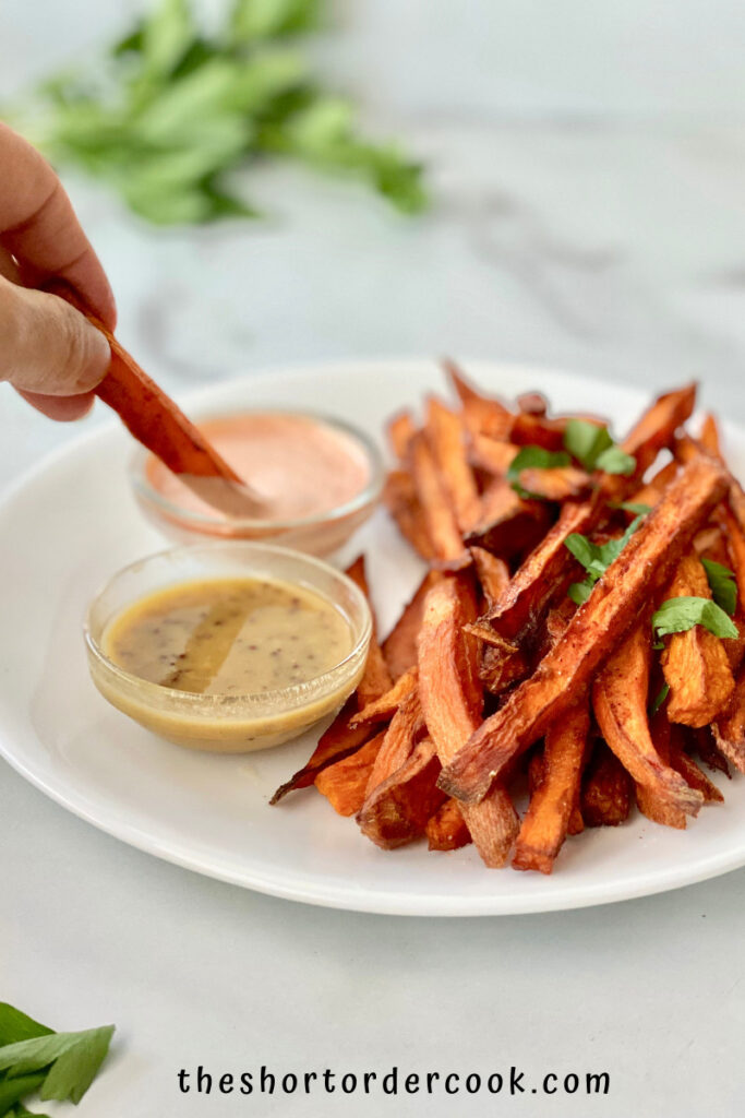 Deep Fried Sweet Potato Fries ready to eat on a plate with hand dipping one into a dipping sauce