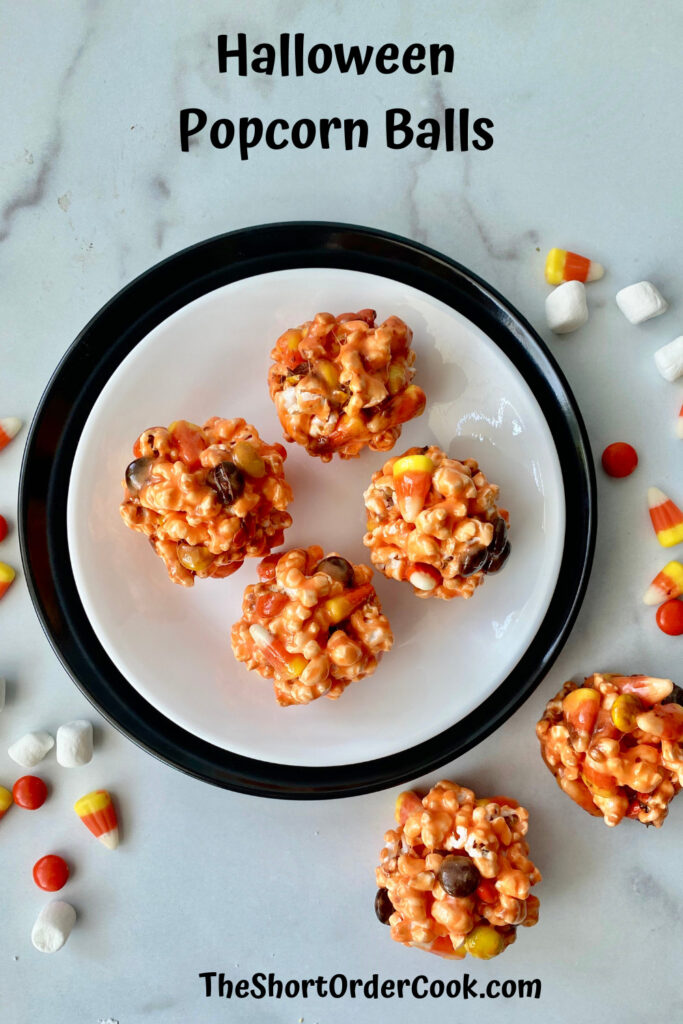 Halloween Popcorn Balls PN1 a plate with 4 orange popcorn balls on it and two more on the counter to the side with a sprinkling of marshmallows and candy
