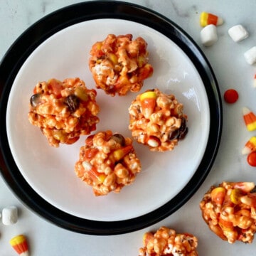 Halloween Popcorn Balls featured overhead of popcorn balls on a plate and some to the side with marshmallows and candy corn on the counter