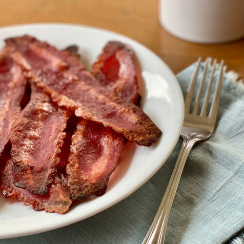 How to Cook Turkey Bacon in the Oven featured plate of cooked bacon to the left with fork napking and mug on the right