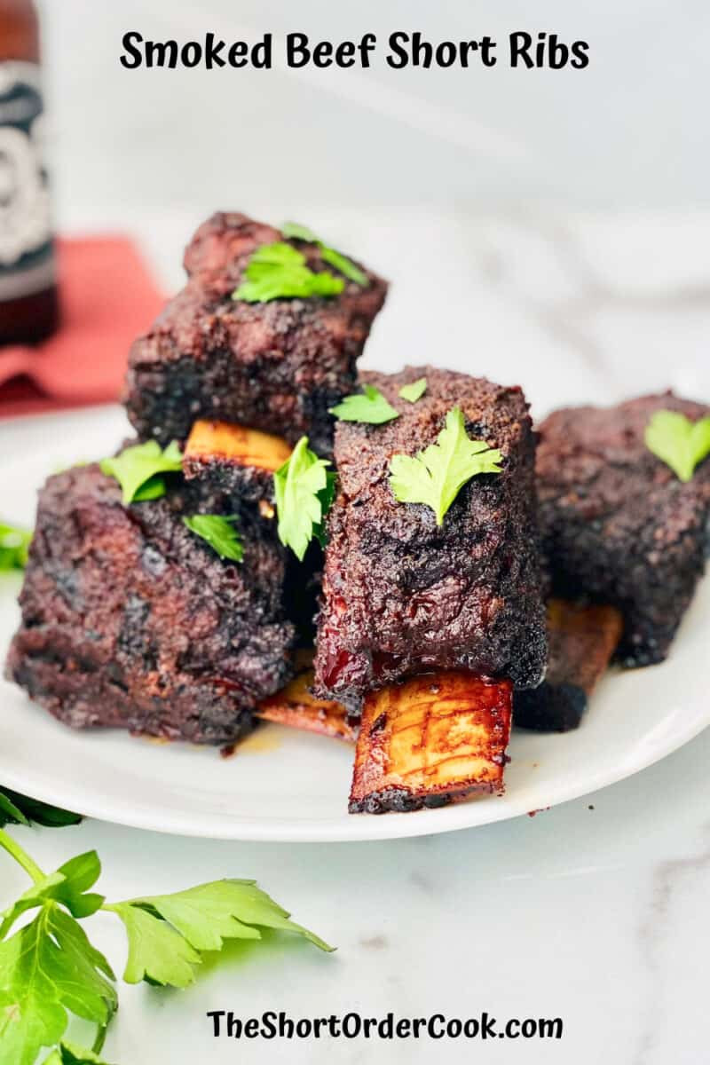 Smoked Beef Short Ribs 5 ribs piled on a plate topped with parsley leaves and parsley and a bottle of beer also on the table