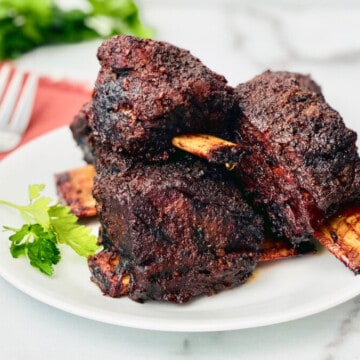 Smoked Beef Short Ribs featured portrait plate of ribs in the center and parsley and napkin utensils in the top left