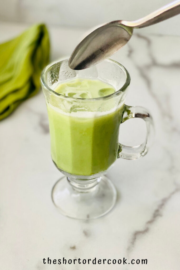 iced Matcha Latte (Starbucks Copycat) spoon stirring in the cup filled with green matcha cream and ice