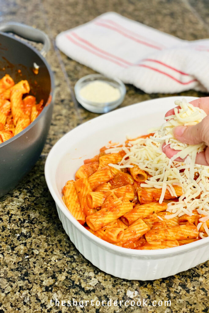 Casserole dish with a layer of sauced pasta and mozzarella be sprinkled over it.