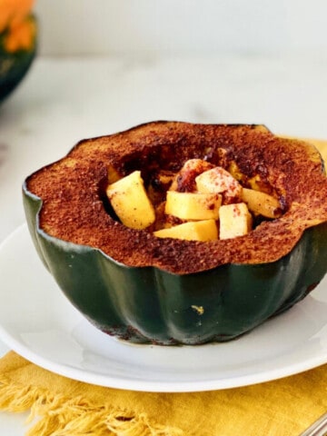 Slow Cooker Brown Sugar Acorn Squash featured plate with half a stuffed squash ready to eat and apple and whole squash in the background