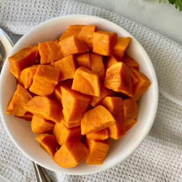 Instant Pot Cubed Sweet Potatoes featured overhead of a bowl filled with cubed sweet potatoes a spoon white linen cloth and fresh parsley