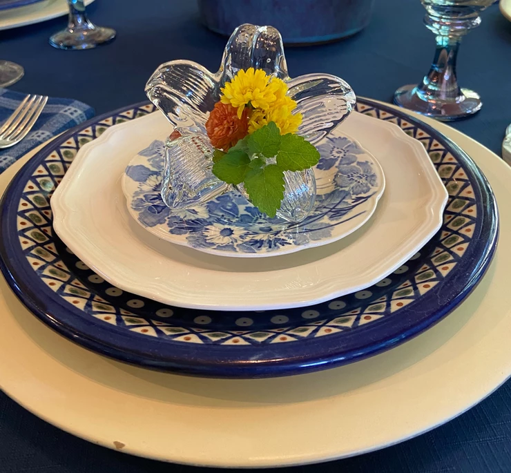 a place setting with white and blue plates atop is the glass vase
with a flower in it