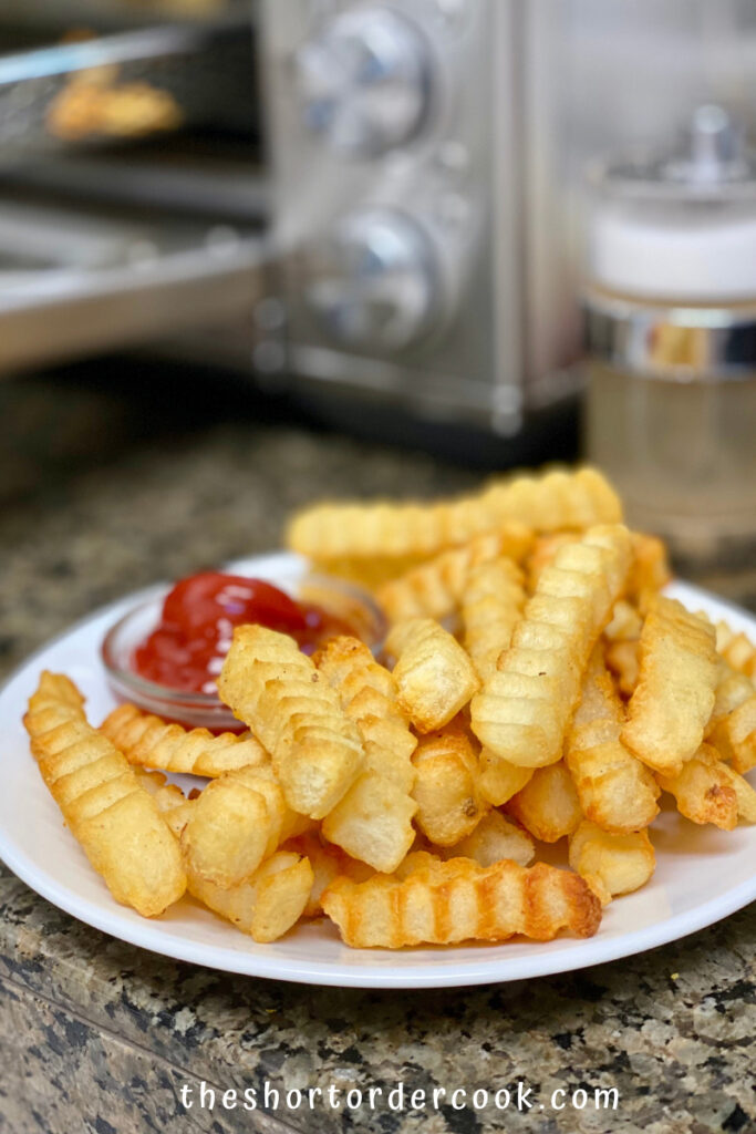 Air Fryer Frozen Crinkle French Fries plated with ketchup in front of the air fryer