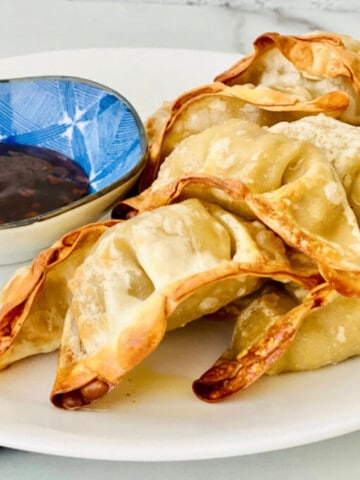Air Fryer Frozen Potstickers featured plated with soy dipping sauce and blue napkin