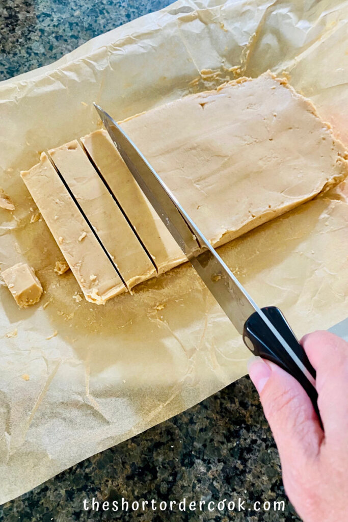 Easy Old-Fashioned Peanut Butter Fudge opened on the parchment paper with a chef knife cutting rows and then cubes