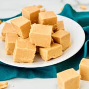 Easy Old-Fashioned Peanut Butter Fudge plate stacked with teal napkin peanutes and fudge on the counter too