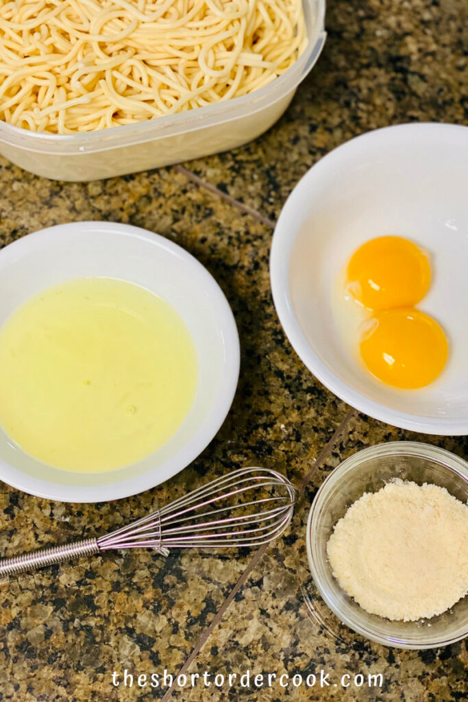 Separated eggs in bowls with whisk and bowl of parmesan cheese plus leftover spaghetti