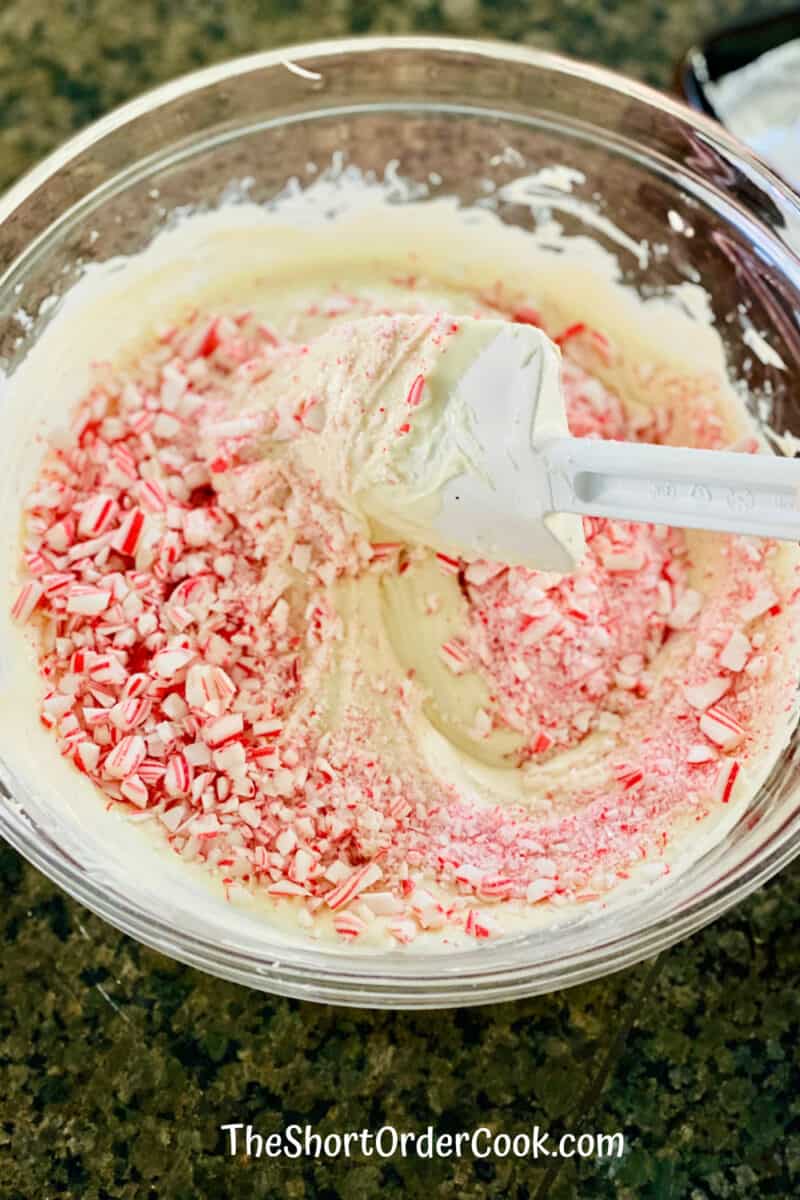 2-Ingredient Peppermint Bark folding the candy cane bits into the melted white chocolate with a silicone spatula