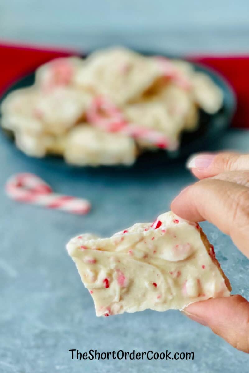 2-Ingredient Peppermint Bark holding a piece plus a plate full in the background