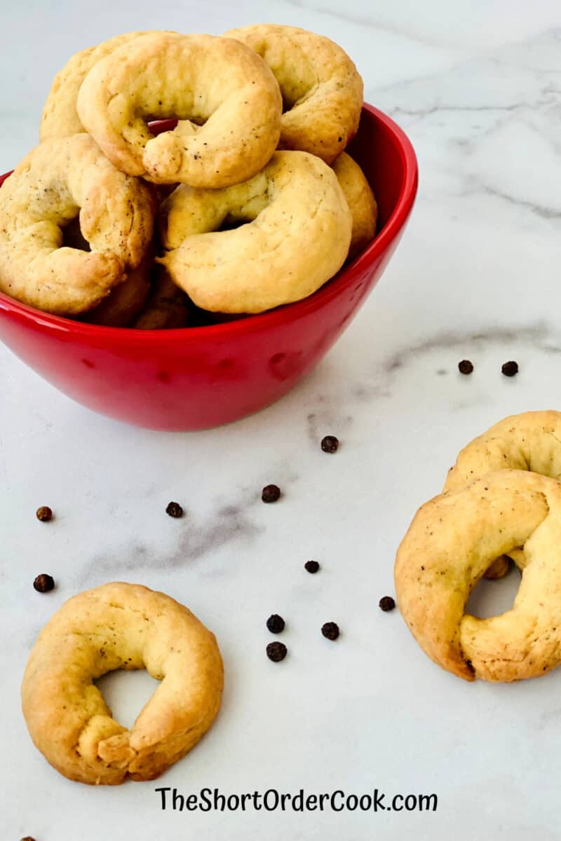 Taralli - Italian Pepper Cookies in a red bowl with a few on the counter with peppercorns