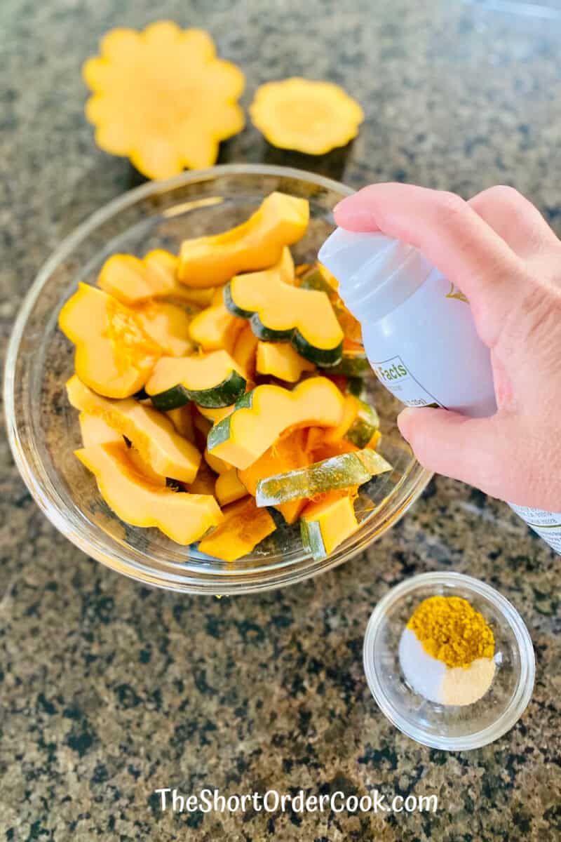 Air Fryer Curried Acorn Squash Slices in a bowl being sprayed with avocado oil