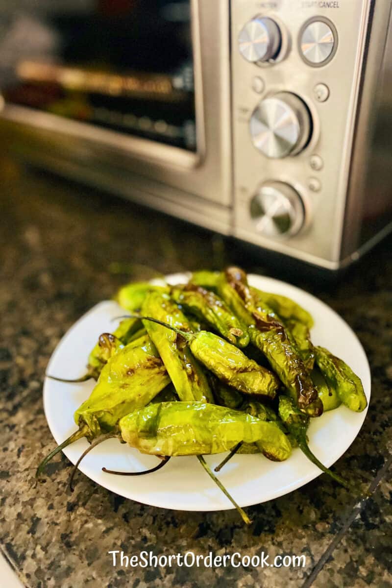 Shishito Peppers on a plate ready to eat in front of the air fryer on the counter