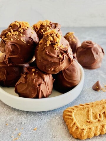 Chocolate-covered Biscoff truffles on a white plate and cookies to the side
