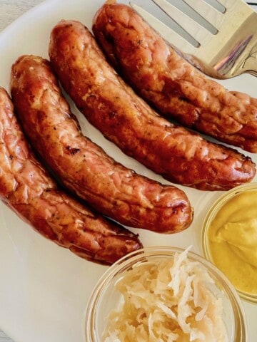 How to Cook Brats in the Oven featured plated brown bratwurst with mustard and kraut