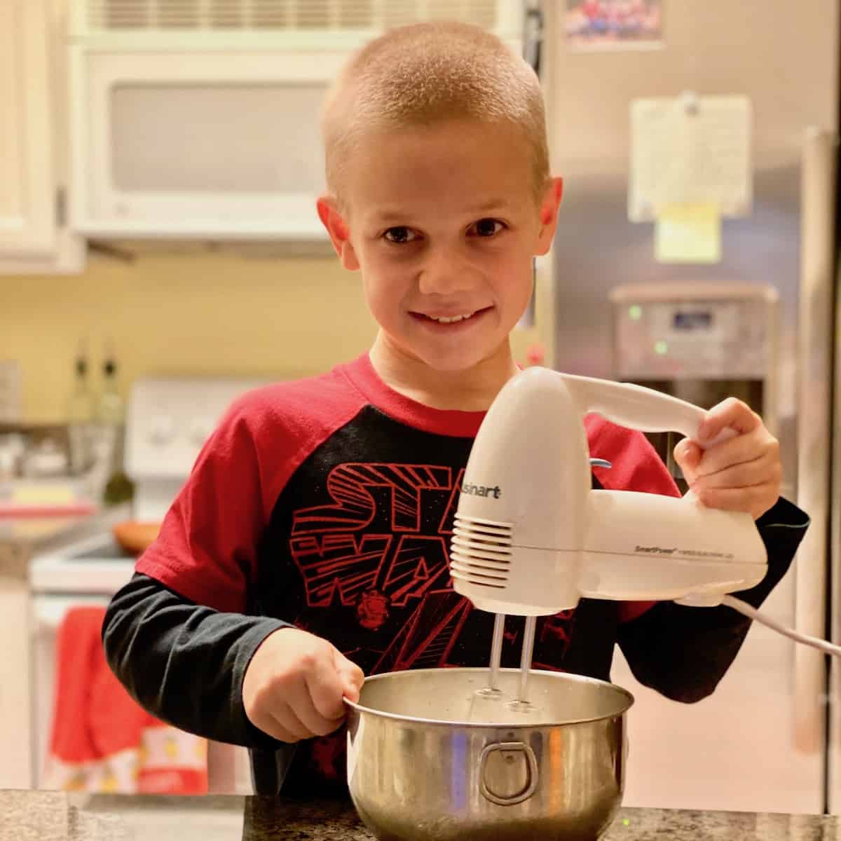 Kid holding a hand mixer whipping up something in a bowl.