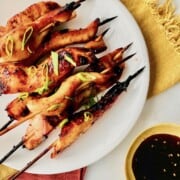Teriyaki chicken on a stick stacked on a plate with dipping sauce