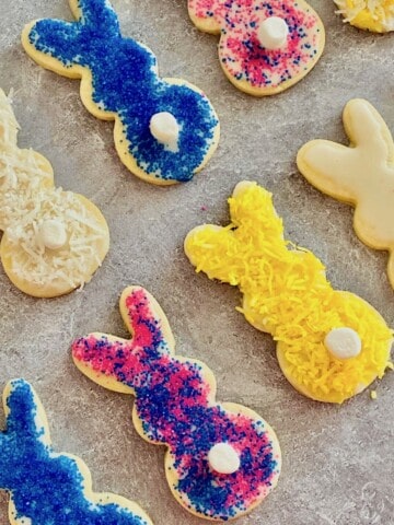 Overhead image of bunny shaped cookies with colored sprinkles or coconut and a mini marshmallow as a cottontail.