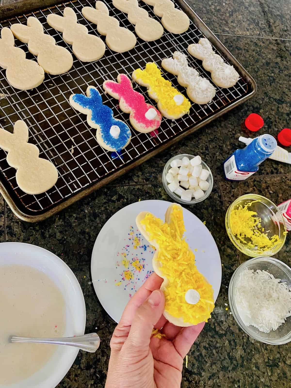 Fully decorated cookie in a hand with decorating ingredients around the counter.
