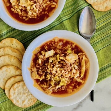 two bowls filled with cabbage roll soup plus crackers and a spoon.