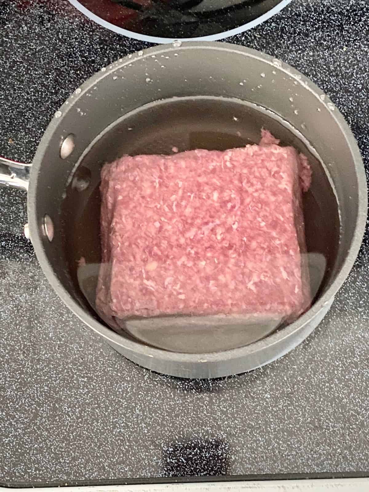 ground beef submerged in water in a pot on the stove